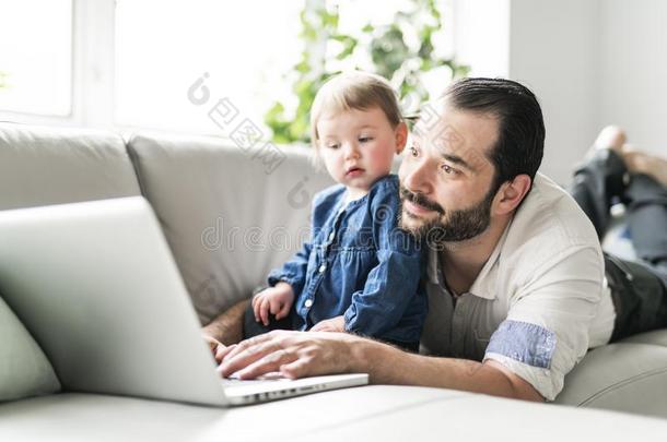 忙碌的父亲工作的向便携式电脑和婴儿采用fr向t