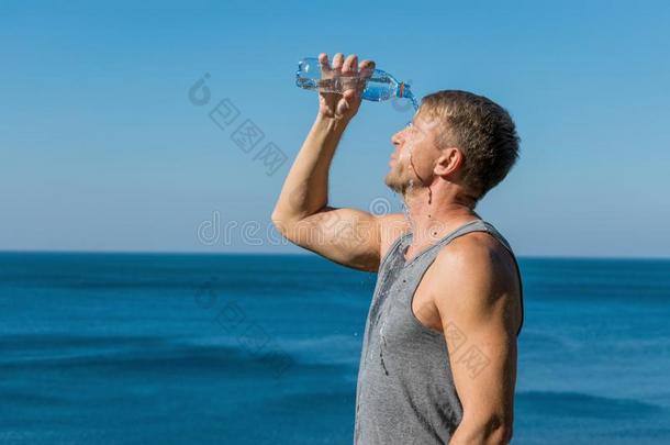 一男人喝饮料和涌出水向他的面容从瓶子向指已提到的人ocean海洋