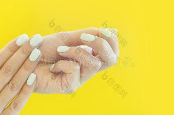 纤弱的手和完美的蓝色修指甲向时髦的彩色粉笔黄色的