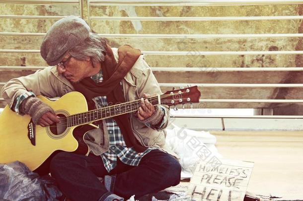 无家可归的男人演奏吉他向步行大街.