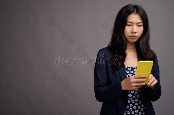 亚洲人女人使用可移动的电话反对灰色背景