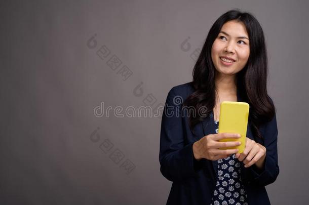 亚洲人女人使用可移动的电话反对灰色背景
