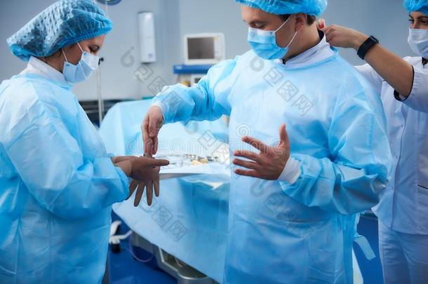仔细的医生放置向橡胶拳击手套在之前指已提到的人外科学