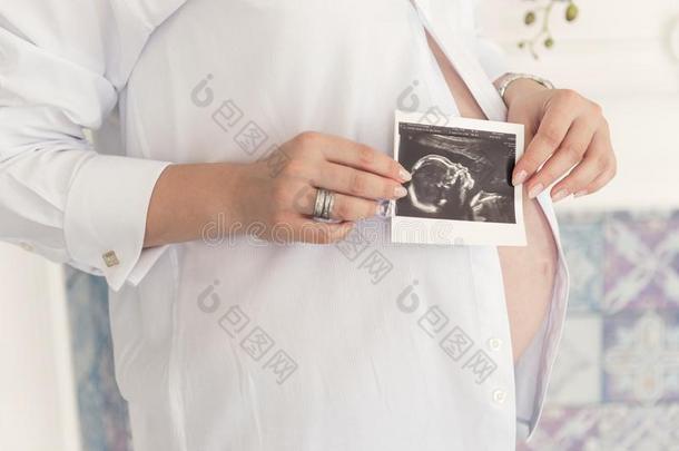 一怀孕的女人和一大的肚子采用一白色的衬衫是（be的三单形式hold采用g一