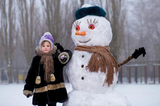 小的欢乐的女孩在近处大的有趣的雪人.漂亮的小的女孩有