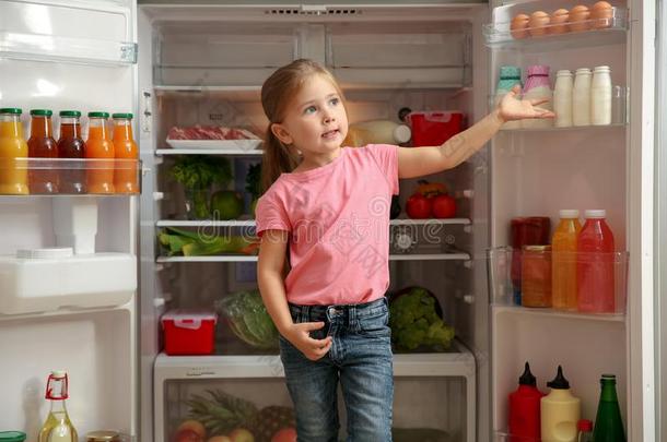 漂亮的小的女孩起立在近处敞开的冰箱