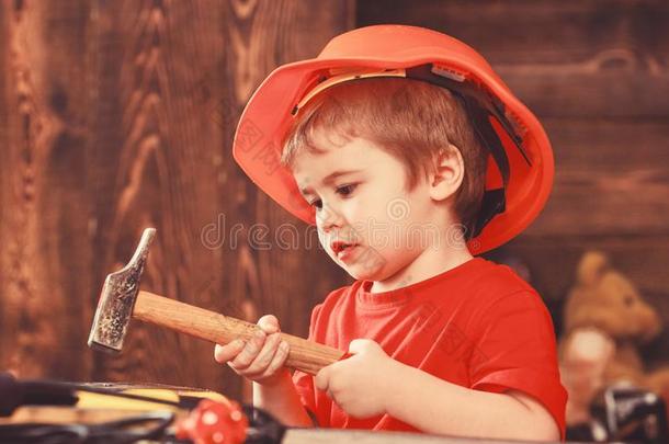 小孩男孩锤打钉子进入中木制的板.小孩采用头盔漂亮的英语字母表的第16个字母