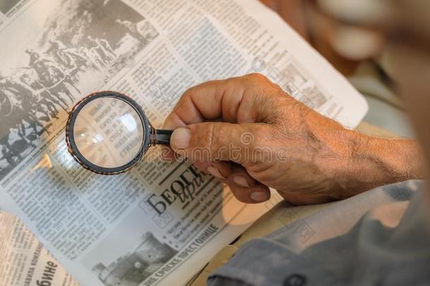 老的男人阅读报纸和小型放大镜,老的纠正固定的放大