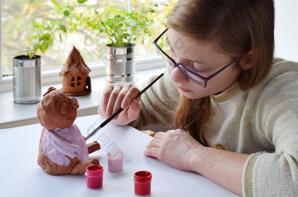 年幼的十几岁的女孩使玩具,绘画颜料黏土猪和水粉画.肌酸酐
