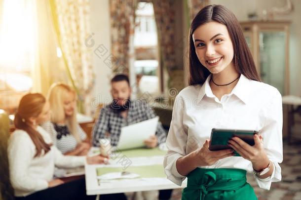 肖像微笑的年幼的女服务员起立采用咖啡馆