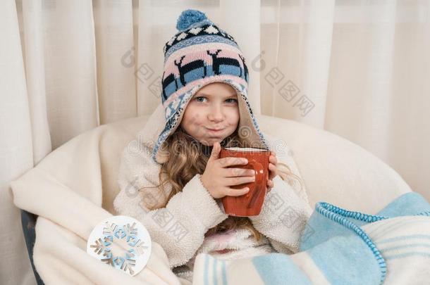 冬时间,小的女孩在家采用一扶手椅和大的杯子关于