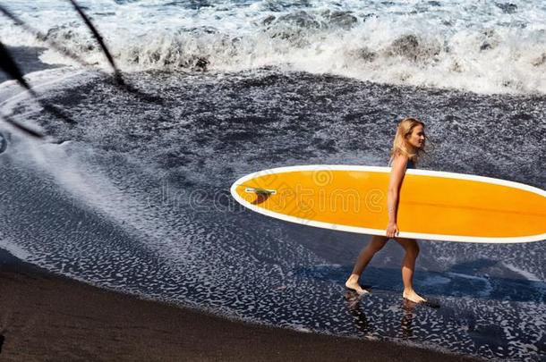 年幼的女人和冲浪板走向黑的沙海滩