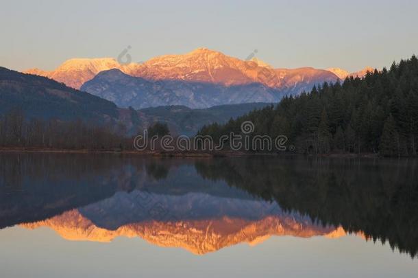 镇定的湖在日落和顶部被雪所盖着的山采用背景