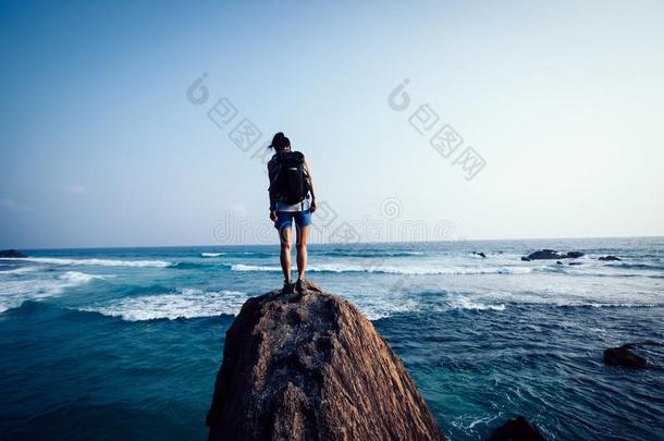 女人背着背包徒步旅行的人向海滨岩石悬崖边
