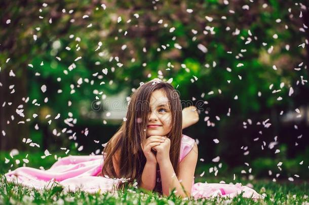 小的女孩向绿色的草和花瓣