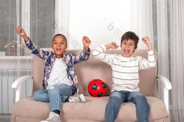 男孩和女孩坐向指已提到的人长沙发椅和注视足球向television电视机.他/她/它们educational-managemen