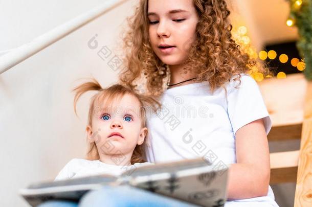 年长的姐妹阅读书高声向她年纪较小者姐妹在楼梯
