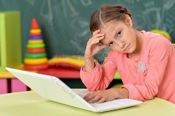 小的女孩使用便携式电脑在期间一次在书桌采用教室