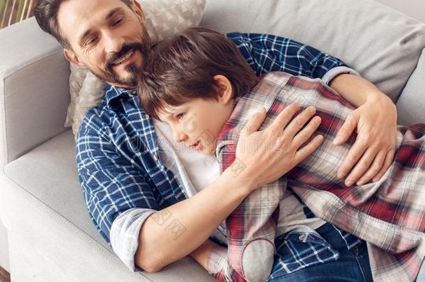 父亲和小的儿子在家说谎向沙发爸爸热烈地拥抱儿子斯米尔