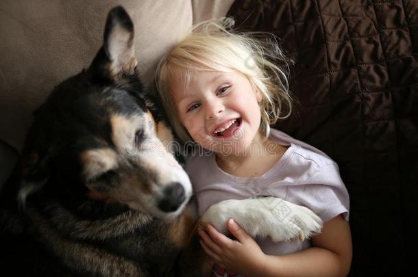 幸福的,笑的小的女孩小孩热烈地拥抱宠物狗向长沙发椅