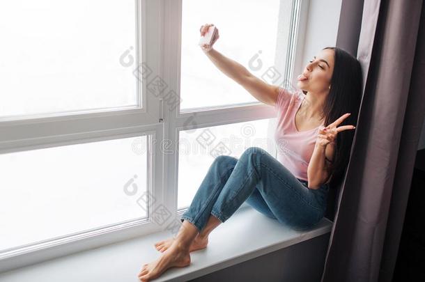 欢乐的年幼的女人拿自拍照在窗.她微笑和使摆姿势.