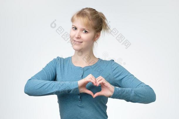 微笑的年幼的女人采用蓝色衬衫show采用g心手势和两个