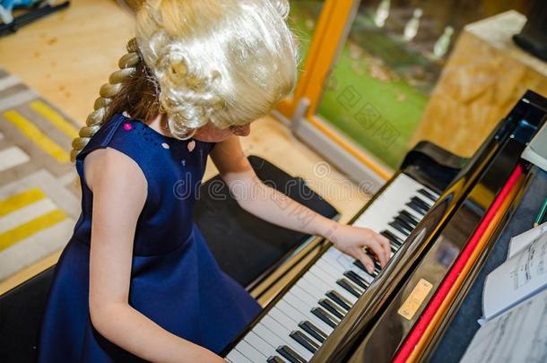 漂亮的小的女孩演奏钢琴,穿衣采用制动火箭莫扎特假发