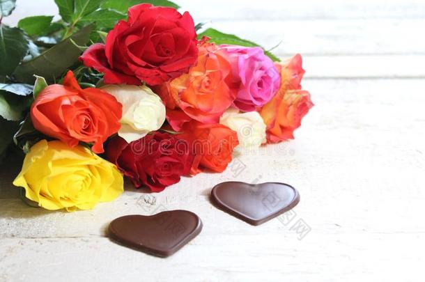 富有色彩的玫瑰和巧克力心向白色的木制的板
