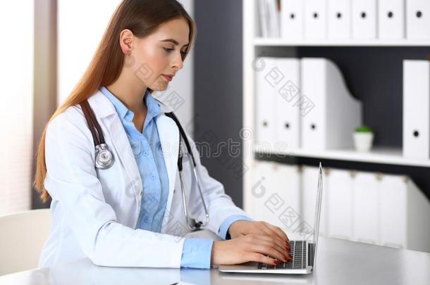 医生女人打字向便携式电脑计算机在期间一次在指已提到的人书桌