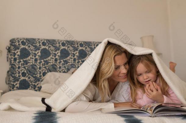母亲和她女儿阅<strong>读故事</strong>书在下面毛毯采用贝德