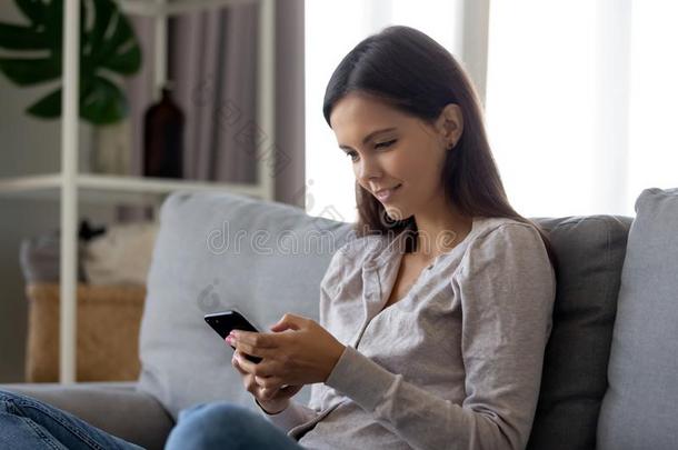 微笑的女孩使用可移动的社会的媒体计算机应用程序一次向长沙发椅