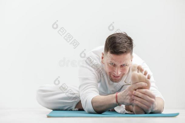 英俊的年幼的男人采用白色的衣服做练习.瑜伽体位法