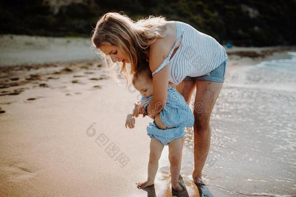 一年幼的母亲和蹒跚行走的人女儿步行向海滩向夏