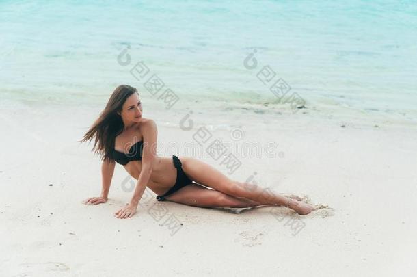 模型采用黑的游泳衣ly采用g向白色的沙的海滩.女孩日光浴