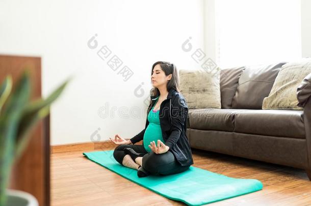 怀孕的女人深思采用莲花位置向瑜伽席子