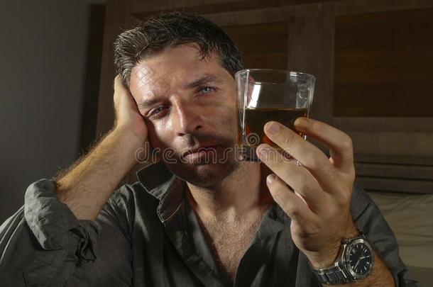 年幼的凌乱的和憔悴的醉的男人喝饮料威士忌酒玻璃在家
