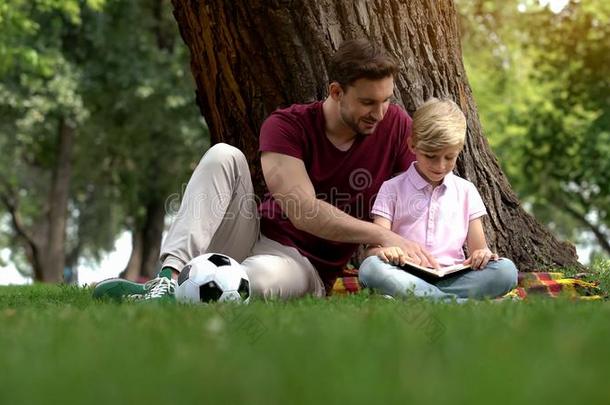 父亲和儿子阅读书采用公园,男人鼓励男孩向知识分子