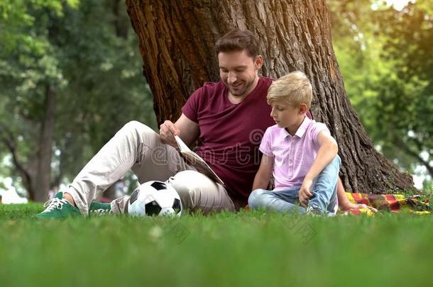 父亲阅读书和儿子采用公园,prepar采用g家庭作业在一起