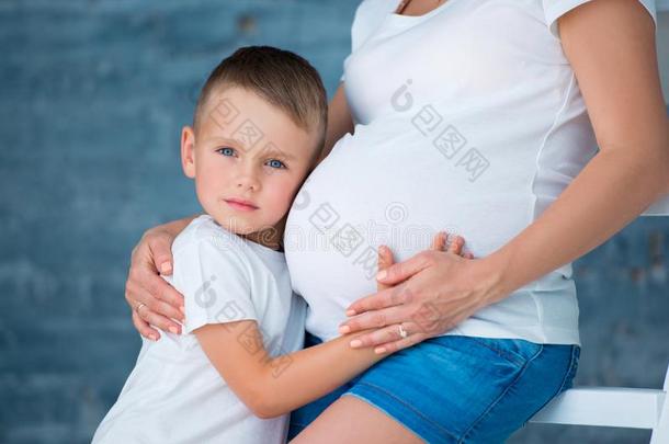 怀孕的妈妈和小的儿子男孩热烈地拥抱肚子.幸福的家庭和