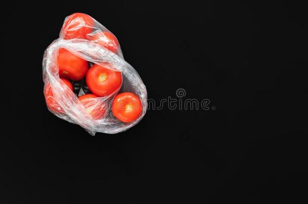 红色的成熟的番茄采用敞开的塑料制品<strong>袋</strong>向黑的背景.