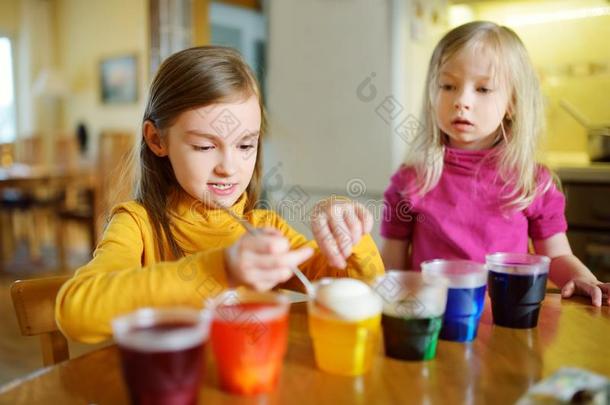 两个漂亮的年幼的姐染色复活节卵在家.孩子们痛苦