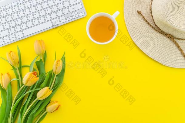 桌面和黄色的郁金香,稻草帽子,茶水杯子和计算机whiteiron白铁
