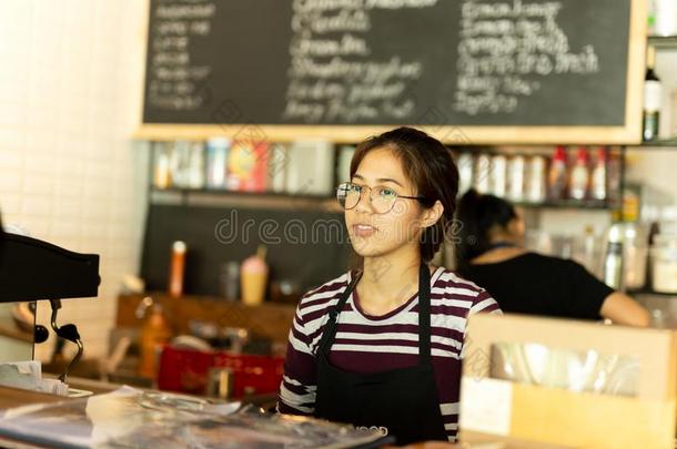 亚洲人女孩和眼镜女服务员使人疲乏的围裙起立采用咖啡