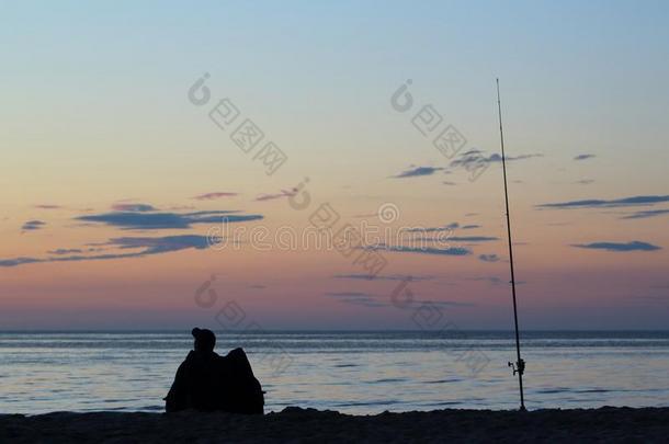 海浪垂钓者和捕鱼杆向指已提到的人波罗的海的海海滩在日落