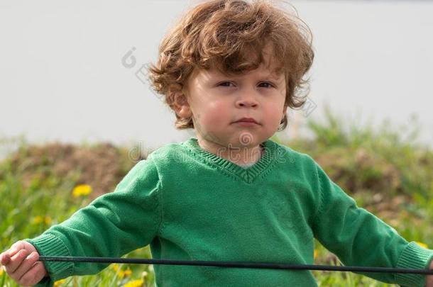 肖像关于年幼的男孩和绿色的毛衣演奏在户外
