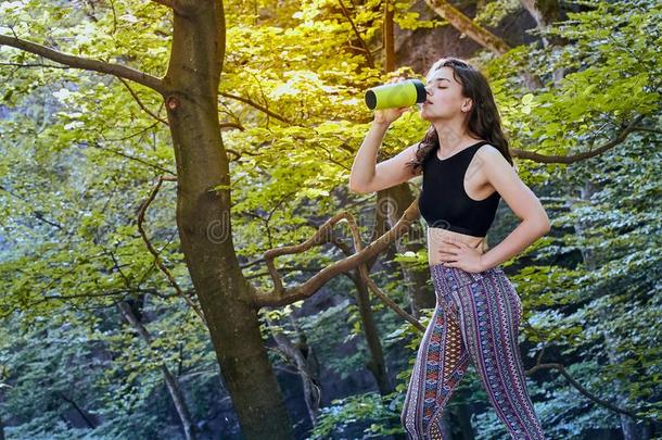 健康的健康女孩喝饮料水从绿色的瓶子采用森林