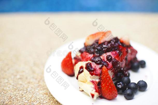 奶油水果蛋白饼蛋糕和新鲜的草莓和越橘的一种向白色的盘子