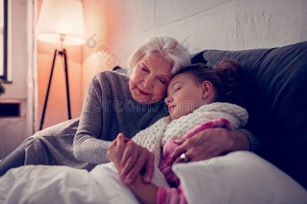 灰色的-有毛发的奶奶热烈地拥抱她恶心的漂亮的女孩落下睡着的