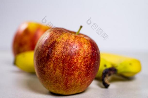 多汁的红色的苹果采用前面关于黄色的香蕉向灰色大理石白色的