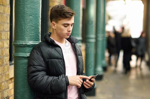 年幼的都市的男人使用智能手机采用都市的背景.